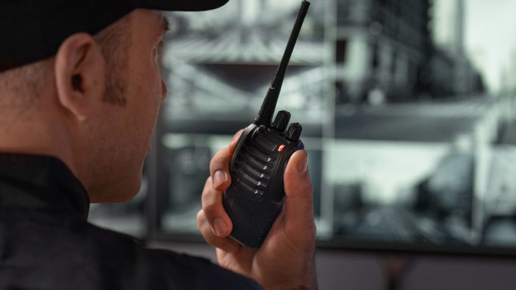 Vigilante de segurança a comunicar por rádio junto a monitores de videovigilância