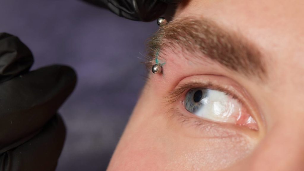Profissional a realizar um piercing na sobrancelha de um cliente