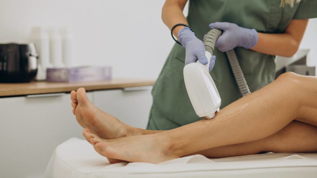 Profissional de estética a realizar depiladação a laser na perna de uma cliente numa clínica