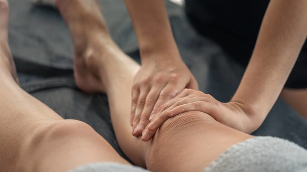 Profissional a realizar uma massagem de drenagem linfática na perna de uma cliente