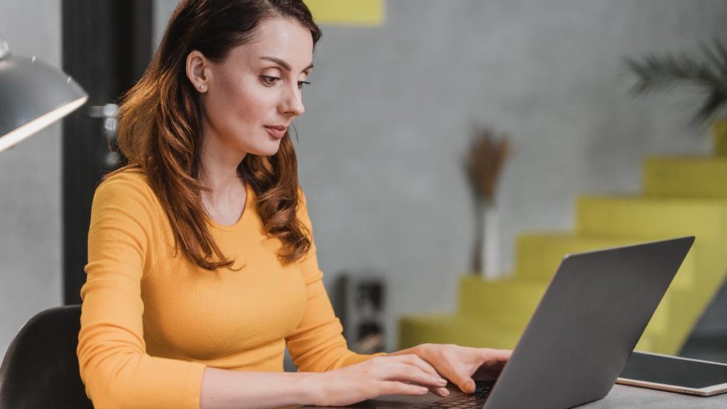 Mulher a trabalhar num computador portátil em casa, a digitar durante uma sessão de e-learning