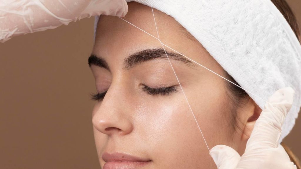 Profissional de estética a realizar depilação à linha (threading) na sobrancelha de uma cliente