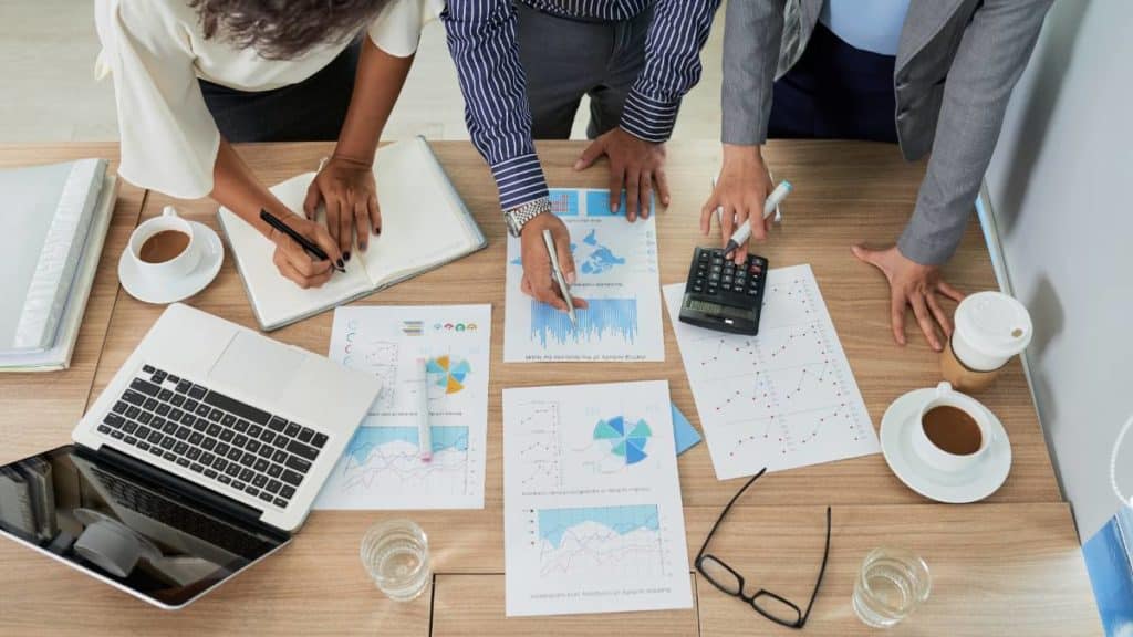 Equipa a analisar gráficos e relatórios financeiros numa mesa de trabalho, vista de cima