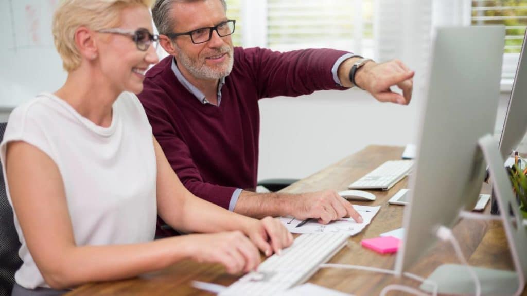 Casal de adultos a aprender informática básica num computador de mesa, com apontamentos ao lado