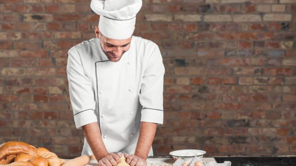Padeiro a amassar massa de pão numa mesa de trabalho, com pães ao lado