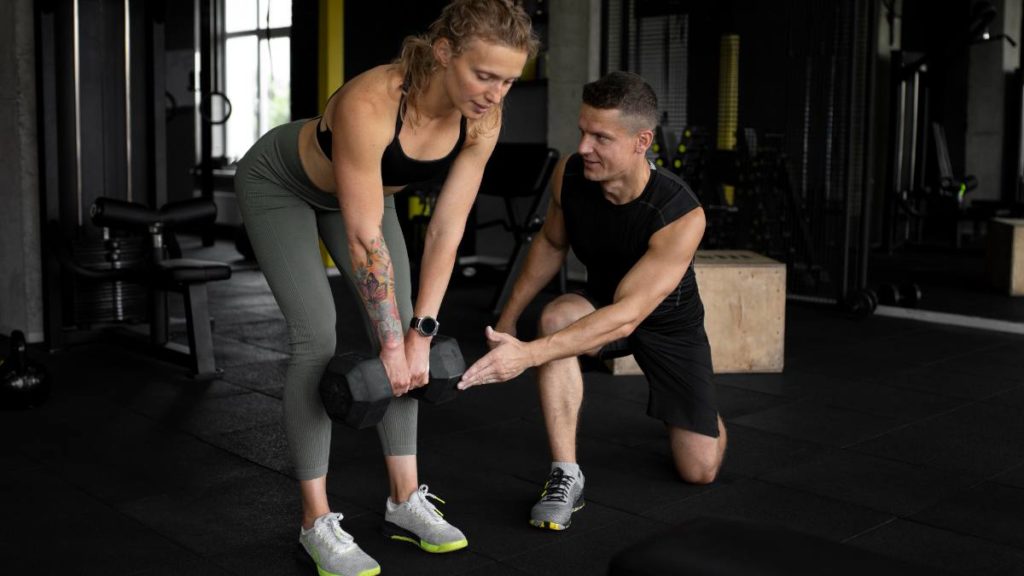 Personal trainer a ajudar uma atleta a levantar um haltere corretamente num ginásio