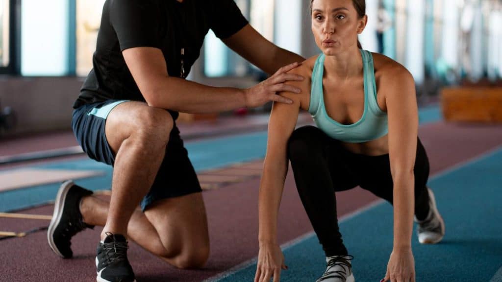 Treinador de exercício físico a orientar a postura de uma atleta numa pista de atletismo
