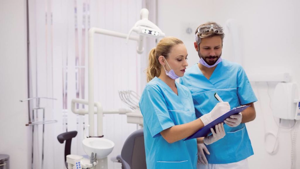Auxiliares de medicina dentária a analisar uma ficha clínica junto ao equipamento odontológico