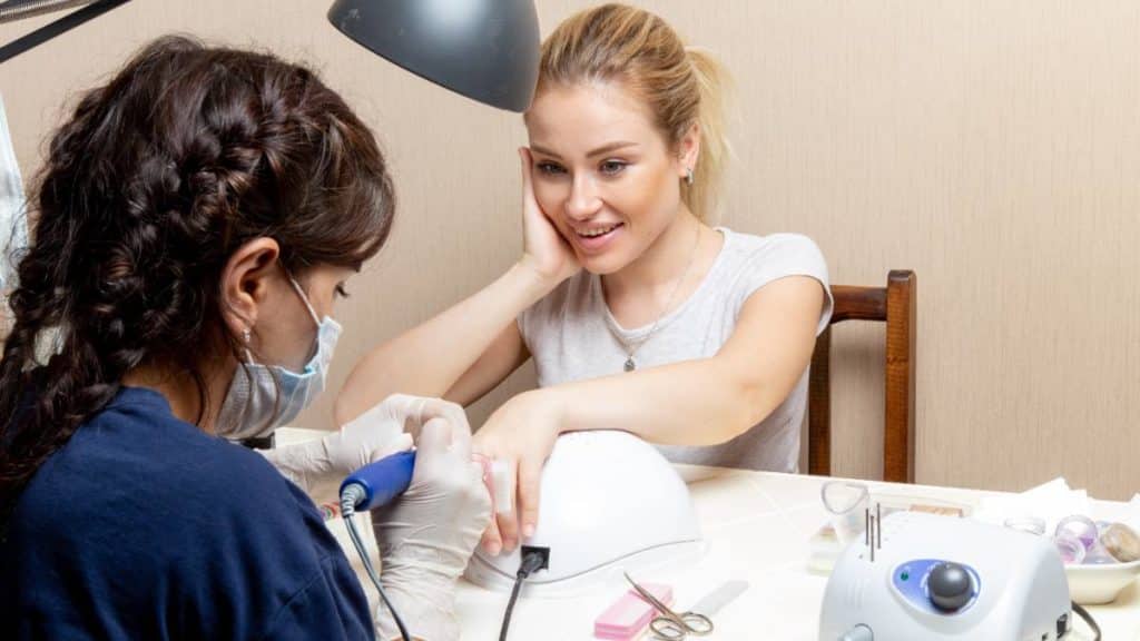 Técnica de estética a fazer unhas em gel a uma cliente numa mesa de trabalho