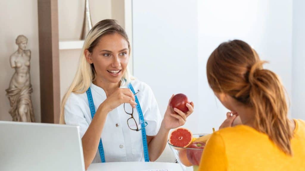 Nutricionista a mostrar uma peça de fruta a uma paciente numa consulta