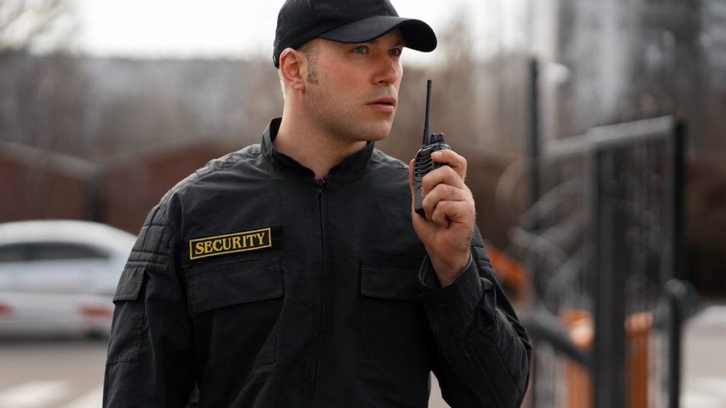 Vigilante de transporte de valores com rádio transmissor, em uniforme de segurança, junto a um portão